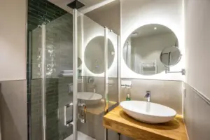 Modernes Badezimmer mit Holzwaschtisch, rundem Spiegel und Glasdusche mit dunklen Fliesen