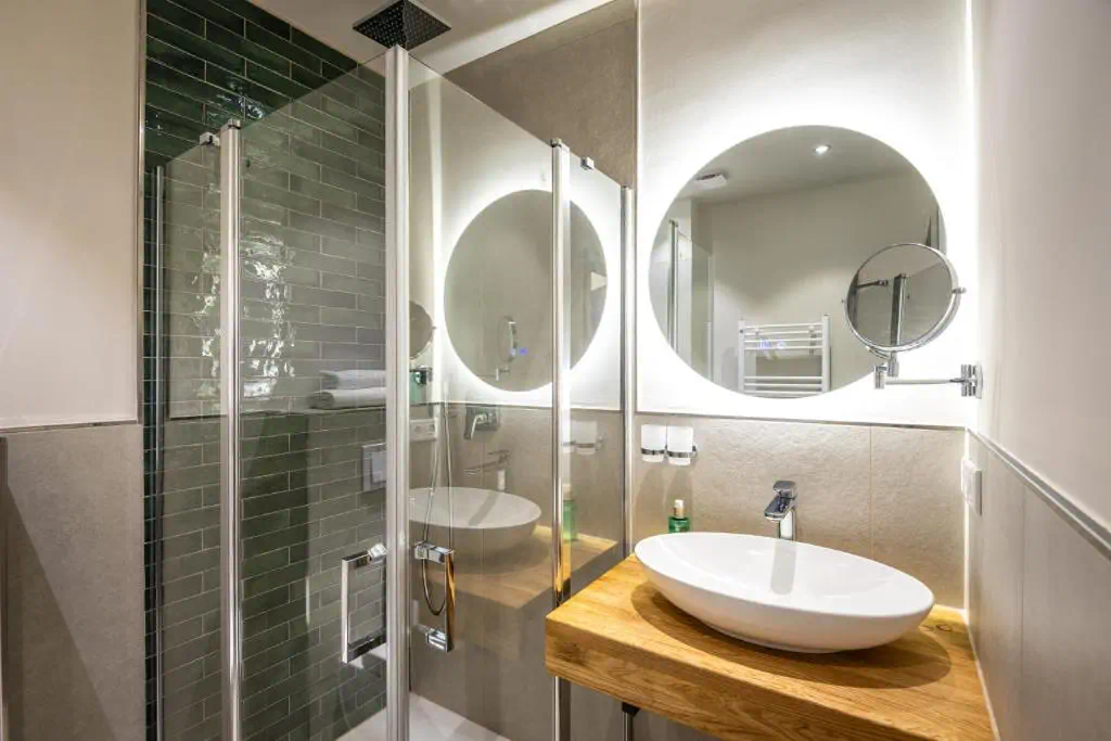 Modernes Badezimmer mit Holzwaschtisch, rundem Spiegel und Glasdusche mit dunklen Fliesen