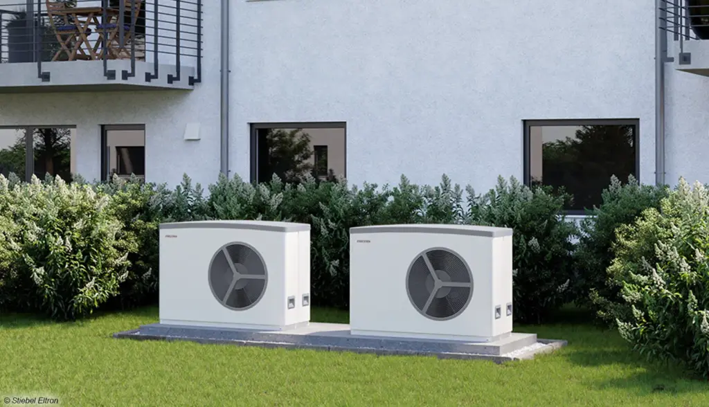 Zwei Wärmepumpen Außengeräte im Garten eines Mehrfamilienhauses energieeffiziente Heizlösung