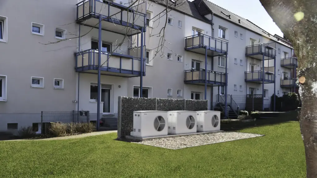 Mehrere Wärmepumpen Außengeräte vor Mehrfamilienhaus zentrale Heizlösung Wohnanlage